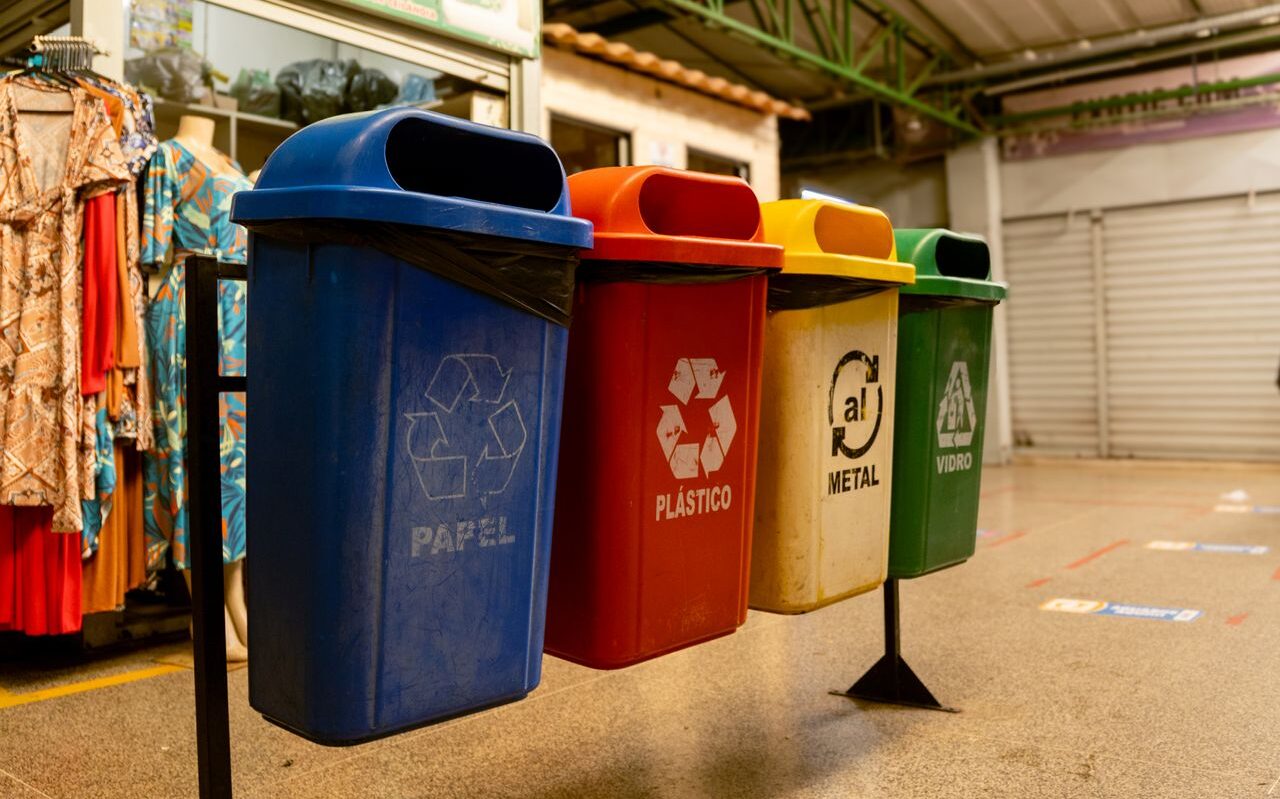 Four recycling bins for paper, plastic, metal, and glass indoors.
